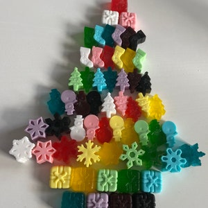 May include: A Christmas tree shaped arrangement of colourful, small, handmade soap bars. The soaps are shaped like Christmas trees, snowflakes, presents, stockings, and snowmen.