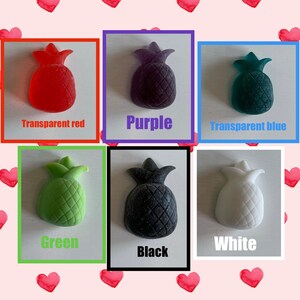 May include: Six pineapple-shaped items in different colours: transparent red, purple, transparent blue, green, black, and white. Each pineapple is presented within a coloured frame, with the colour name below. The background has a pattern of red hearts.