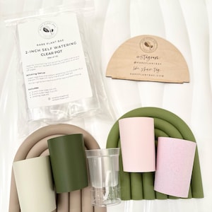 May include: A selection of self-watering clear pots, with a set of 10, and wicking setup. The image includes a clear plastic pot, and several coloured pots in green, pink, and beige. A wooden sign and a plastic bag with text are also included.