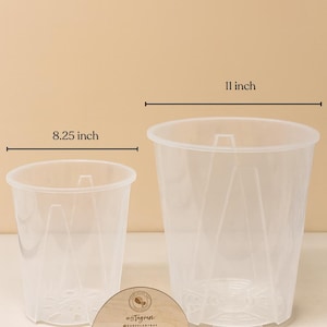 May include: Two clear plastic plant pots, one 8.25 inches wide and the other 11 inches wide. The pots have a tapered design with drainage holes. A wooden sign with social media information is in front of the pots.