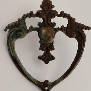 May include: A heart-shaped antique cabinet pull with a decorative, ornate design. The pull is made of metal and has a green patina finish.