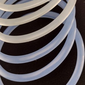 May include: Close-up of several light blue and white rubber O-rings. The rings are stacked on top of each other, with the light blue rings at the bottom and the white rings at the top. The rings are made of a flexible material.