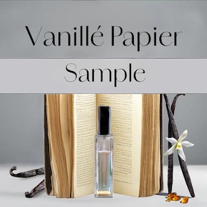 May include: A perfume sample bottle with a black cap stands before an open antique book. The image includes vanilla beans, a white vanilla flower, and the text "Vanillé Papier Sample".
