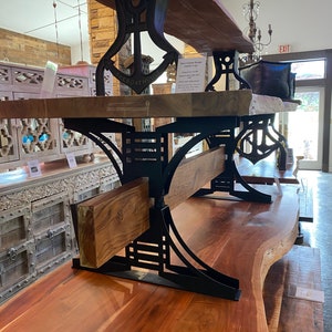 May include: A wooden table with a live edge top and black metal anchor-shaped legs. The table is made by The Boathouse and has a rustic, industrial style.