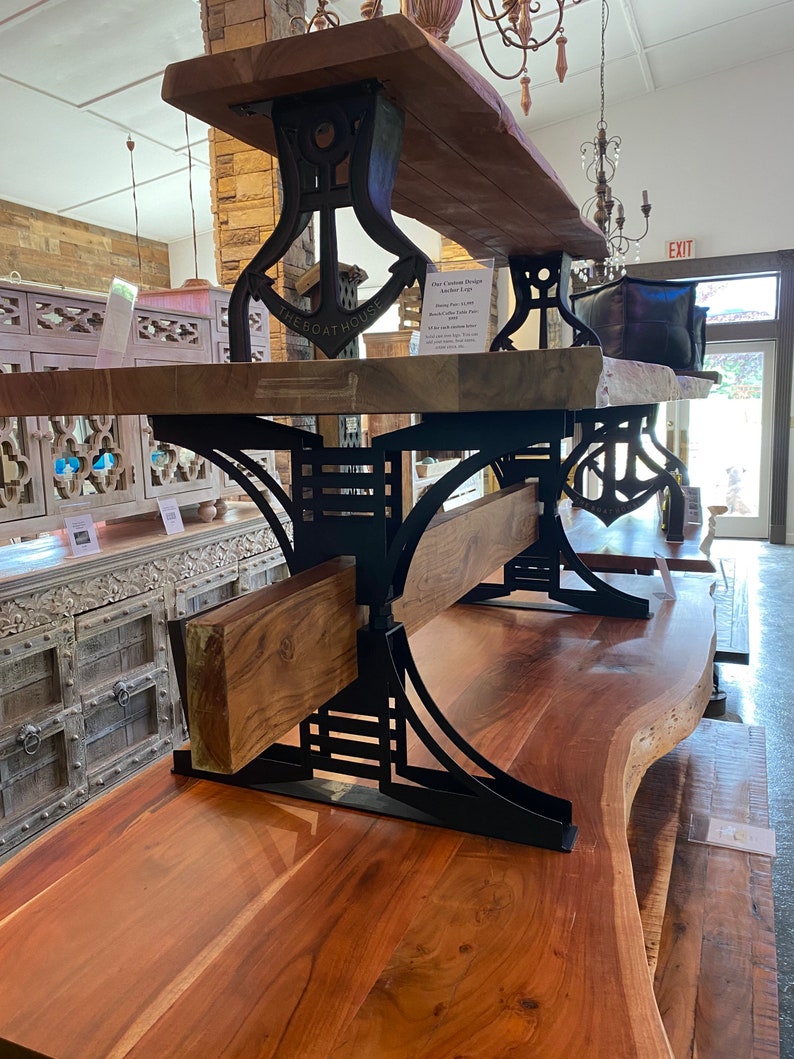 May include: A wooden table with a live edge top and black metal anchor-shaped legs. The table is made by The Boathouse and has a rustic, industrial style.