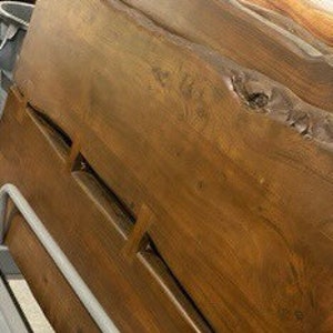 May include: A large, dark brown wooden headboard with a live edge and natural wood grain. The headboard has a unique, organic shape with a large knot in the wood.
