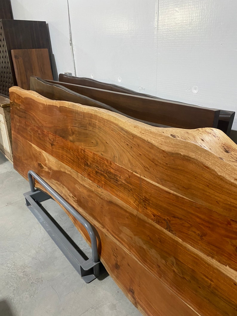 May include: A large, rustic wooden slab with a live edge. The slab is a rich brown color with a natural wood grain pattern. It is supported by a gray metal stand.