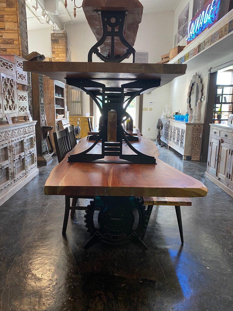 May include: A large wooden dining table with a live edge top and black metal industrial style base. The table is made of reclaimed wood and has a rustic look. The base is made of heavy-duty metal and has a gear design.