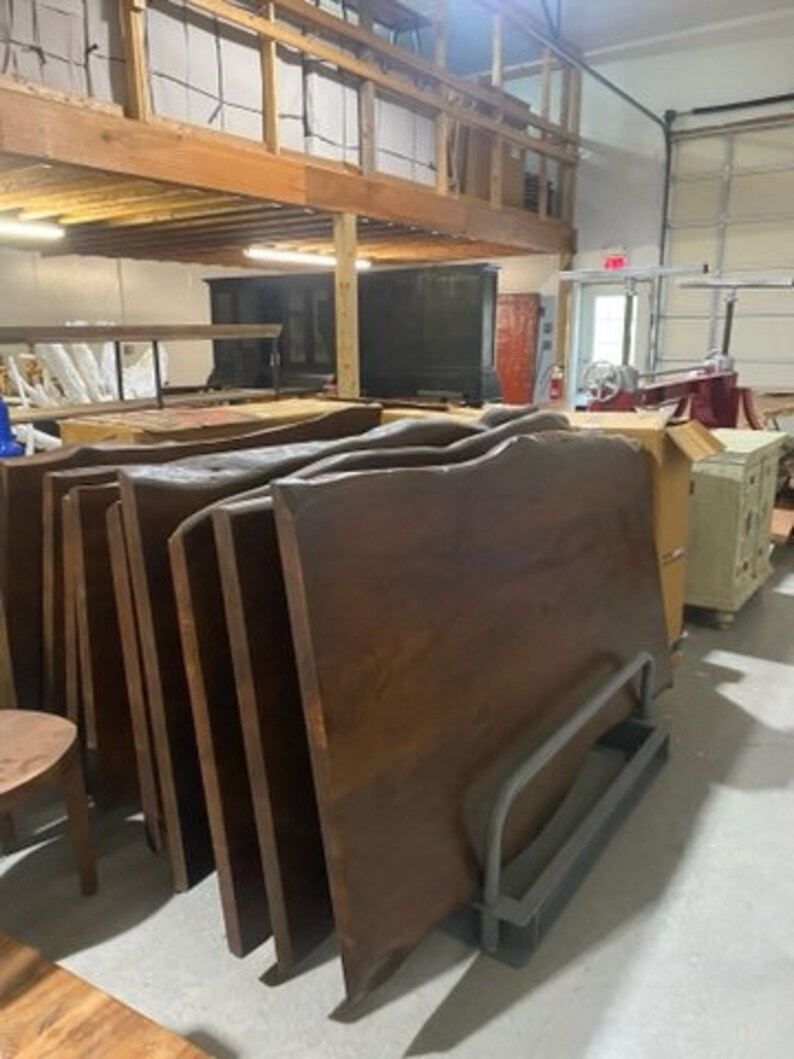 May include: A stack of large, dark brown wooden slabs with a live edge. The slabs are stacked on top of each other and are leaning against a wall. The slabs are likely for use as tabletops or countertops.