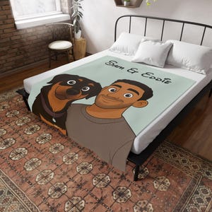 May include: A light blue blanket with a cartoon illustration of a man and a dog, a Rottweiler. The blanket has the text "Sam & Eddie" in black script. The blanket is on a bed with white pillows.