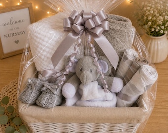 Può includere: Un cesto regalo avvolto in cellophane trasparente con un fiocco grigio contenente una coperta bianca a nido d'ape, una coperta grigia, un peluche a forma di elefante grigio, un paio di scarpine in maglia grigie e tre fasce avvolgenti arrotolate.