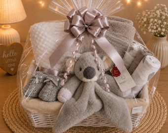 Può includere: Un cesto regalo avvolto in cellophane trasparente con un fiocco grigio contenente un peluche koala tipo copertina di sicurezza, una coperta bianca con trama a cialda, una coperta grigia, scarpine lavorate a maglia grigie e tre mussole arrotolate.