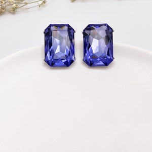 May include: A pair of blue gemstone earrings with a square cut. The earrings are set in silver.