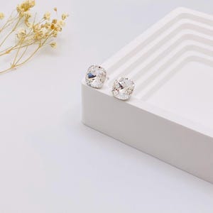 May include: A pair of silver stud earrings with clear square-shaped crystals.