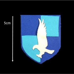 May include: A blue and turquoise felt crest with a white eagle design. The crest is approximately 5 cm tall.