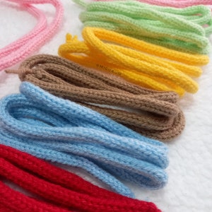 May include: A collection of colourful crocheted cords in pink, green, yellow, brown, blue and red. The cords are arranged in a row, with the pink cord at the top and the red cord at the bottom.