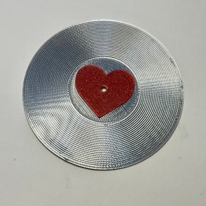 May include: A silver-colored vinyl record with a red heart in the center.