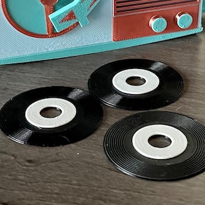 Könnte beinhalten: Drei schwarze Vinyl-Untersetzer mit weißen Mittelpunkten. Die Untersetzer befinden sich auf einer dunklen Holzoberfläche.