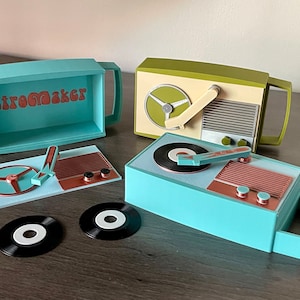 Op de afbeelding: Een set van drie turquoise en groene retro-platenspelers met een plaat en een naald. De platenspelers zijn gelabeld met "Retromaker".