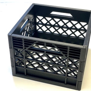 Puede incluir: Una caja de plástico negra con un patrón de rejilla. La caja está vacía y tiene un asa en la parte superior.