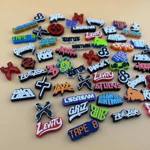 May include: A collection of colorful shoe charms featuring various logos and text, including "Levity", "LSDream", "Tape B", "Virtual Riot", "Zingara", "Boogie T", "Level Up", "Giant Nightmare", "Griz", and "Atliens".
