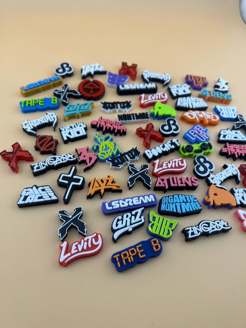 May include: A collection of colorful shoe charms featuring various logos and text, including "Levity", "LSDream", "Tape B", "Virtual Riot", "Zingara", "Boogie T", "Level Up", "Giant Nightmare", "Griz", and "Atliens".