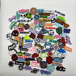 May include: A collection of colorful, round, and square stickers with various music artist names and logos. The stickers feature a variety of designs, including cartoon characters, geometric shapes, and text.