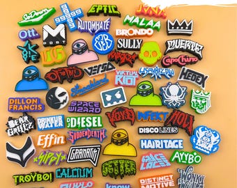 May include: A collection of colorful shoe charms with various designs and text, including the words "Bass Variety!!!", "Ott", "Dillon Francis", and "99999". The charms feature a variety of shapes and colors, with some displaying cartoon-like characters.
