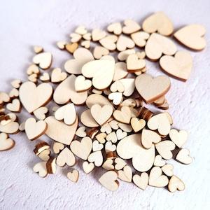 May include: A large pile of wooden hearts of various sizes, arranged in a heart shape. The hearts are a light brown colour and have a smooth, natural finish.