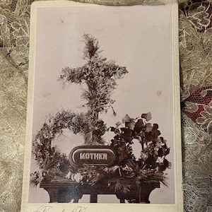 May include: A sepia-toned photograph featuring a floral cross and wreath arrangement. The word "MOTHER" is displayed on an oval plaque. The photograph is framed with the text "Fred Bremer, Greenville, Mich."