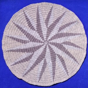 May include: A round crocheted rug with a spiral design in shades of gray and beige.