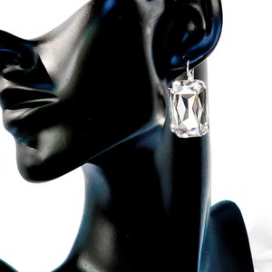 May include: A pair of silver earrings with large, clear, rectangular crystal stones.