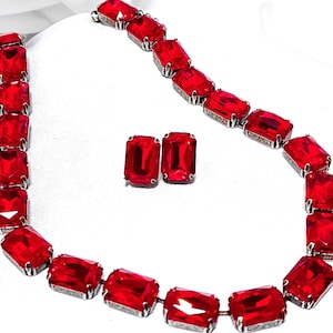 Peut inclure: Un collier et des boucles d'oreilles en strass rouge. Le collier est composé d'une chaîne de strass rouges rectangulaires. Les boucles d'oreilles sont également des strass rouges rectangulaires.