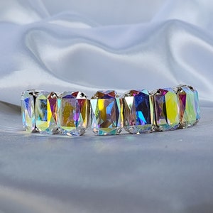 May include: A shimmering bracelet featuring rectangular, iridescent crystals set in a silver-toned metal. The crystals reflect a spectrum of colors, including yellow, pink, and blue, creating a dazzling effect. The bracelet is designed to stretch.