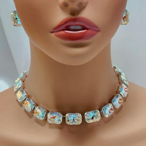 May include: A dazzling jewelry set featuring a necklace and matching earrings. The set showcases large, rectangular iridescent crystals set in a silver-tone metal. The necklace sits elegantly around the neck, while the earrings are square-shaped.
