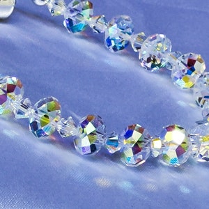 Puede incluir: Un brazalete de cristal con cuentas iridiscentes. El brazalete está hecho de cuentas de cristal transparente con un diseño facetado. Las cuentas están enhebradas en una cadena de plata.
