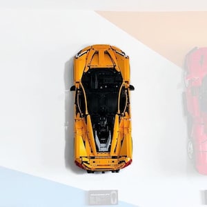 May include: A yellow Lego model car with black detailing, viewed from above. The car is on a white surface with a blue and orange background.