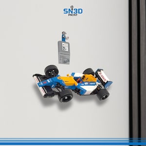 May include: A blue, yellow, and white toy race car with black wheels. The car has sponsor logos and is mounted on a wall. A gray 3D-printed object with the text "SN3D PRINT" is also mounted on the wall.