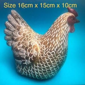 May include: A brown and white chicken figurine with a red comb and wattle, featuring detailed feather patterns. The text "Size 16cm x 15cm x 10cm" is printed at the top. The chicken is depicted in profile, showcasing its textured plumage and beak.