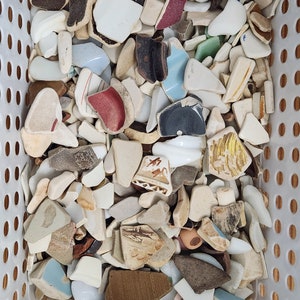 May include: A white basket filled with a variety of broken ceramic pieces. The pieces are in various shapes and sizes, and some have colourful designs.