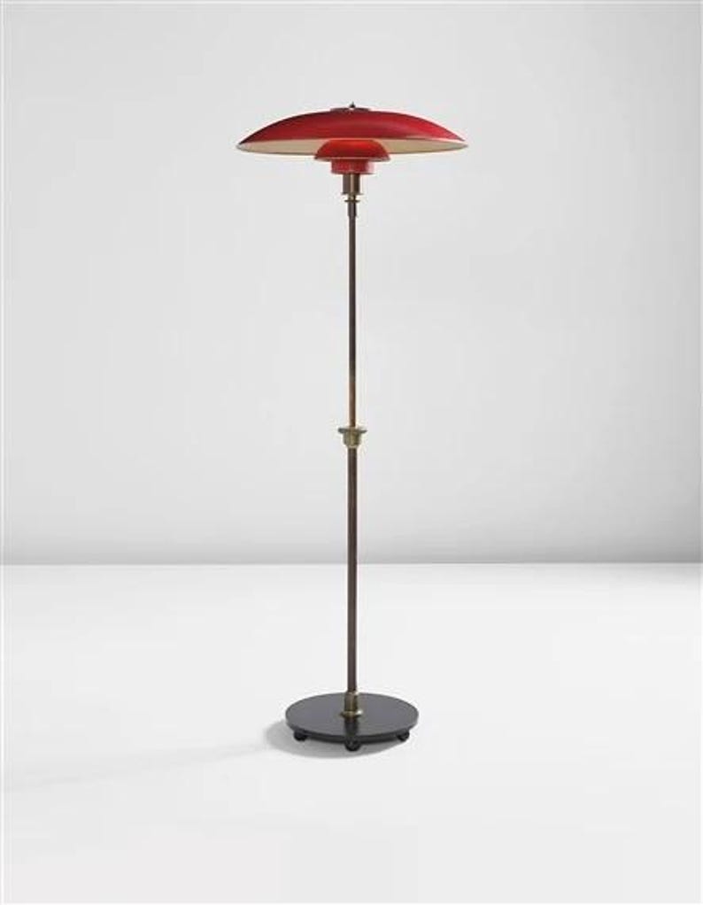 May include: A red and white floor lamp with a round, flat shade and a black base. The lamp has a long, thin stem and is on wheels.