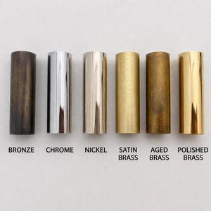 Op de afbeelding: Zes cilindervormige metalen onderdelen op een rij, met verschillende afwerkingen gelabeld als brons, chroom, nikkel, gesatineerd messing, verouderd messing en gepolijst messing. Elke cilinder heeft een gladde, verticale oriëntatie.