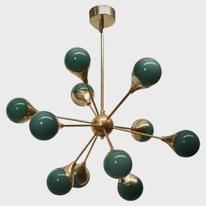 May include: A mid-century modern chandelier with a brass finish and green globe shades. The fixture has multiple arms extending from a central sphere, each holding a green globe with a brass accent. The design is reminiscent of atomic age aesthetics.
