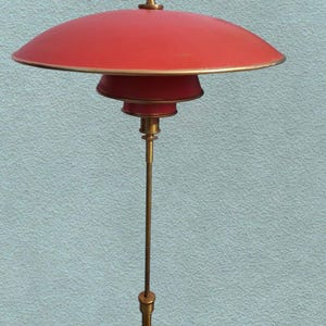 May include: A red and gold floor lamp with a wide, saucer-shaped shade. The lamp has a tall, slender base and a simple design.
