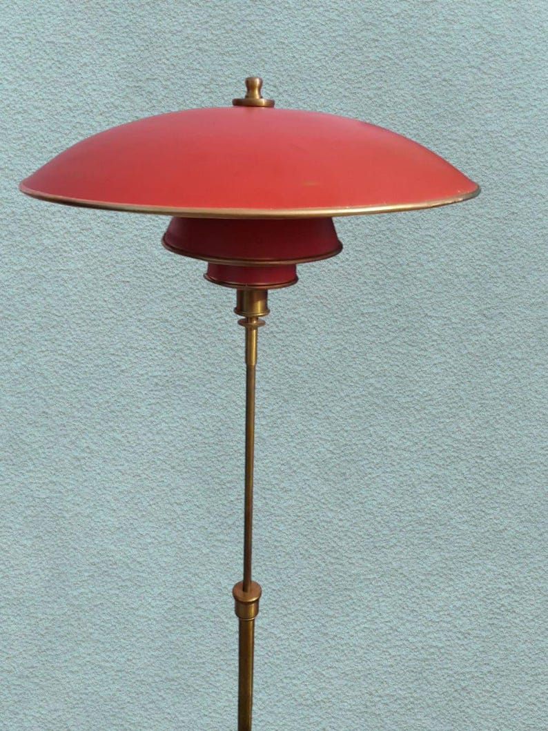 May include: A red and gold floor lamp with a wide, saucer-shaped shade. The lamp has a tall, slender base and a simple design.