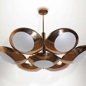 May include: A gold-toned chandelier with six circular lights, each with a white frosted glass shade. The chandelier has a modern mid-century design.
