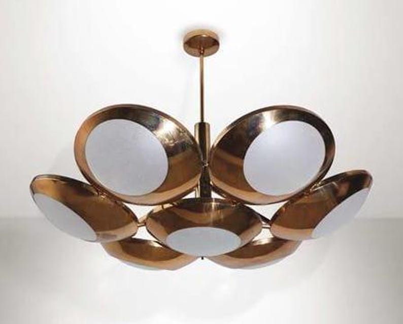 May include: A gold-toned chandelier with six circular lights, each with a white frosted glass shade. The chandelier has a modern mid-century design.