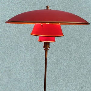 May include: A red and gold floor lamp with a large, round, red shade and a smaller, round, red shade. The lamp has a long, thin, gold stem.