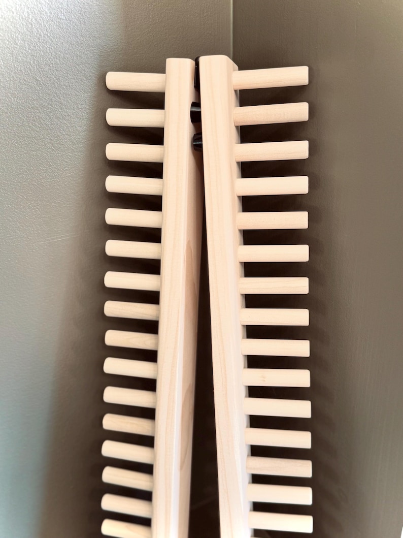 Op de afbeelding: Twee houten stropdashouders, elk met meerdere horizontale deuvels, worden getoond tegen een neutrale achtergrond. De houders zijn gemaakt van lichtgekleurd hout en zijn aan de bovenkant scharnierend. De deuvels zijn gelijkmatig verdeeld.