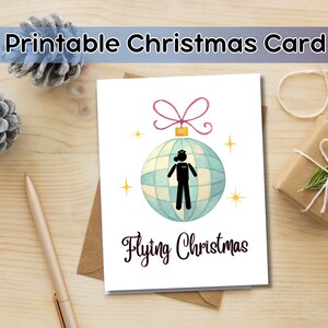 May include: A printable Christmas card with a watercolor-style disco ball ornament design. The ornament features a stick figure in a pilot's uniform. The words "Flying Christmas" are written below the ornament.
